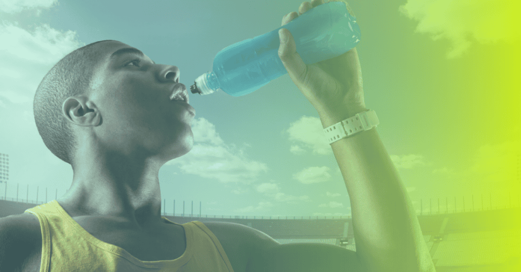 A person wearing a tank top drinks from a sports bottle at an outdoor stadium, with a bright sky in the background—embracing the spirit of corporates wellness and healthy living.