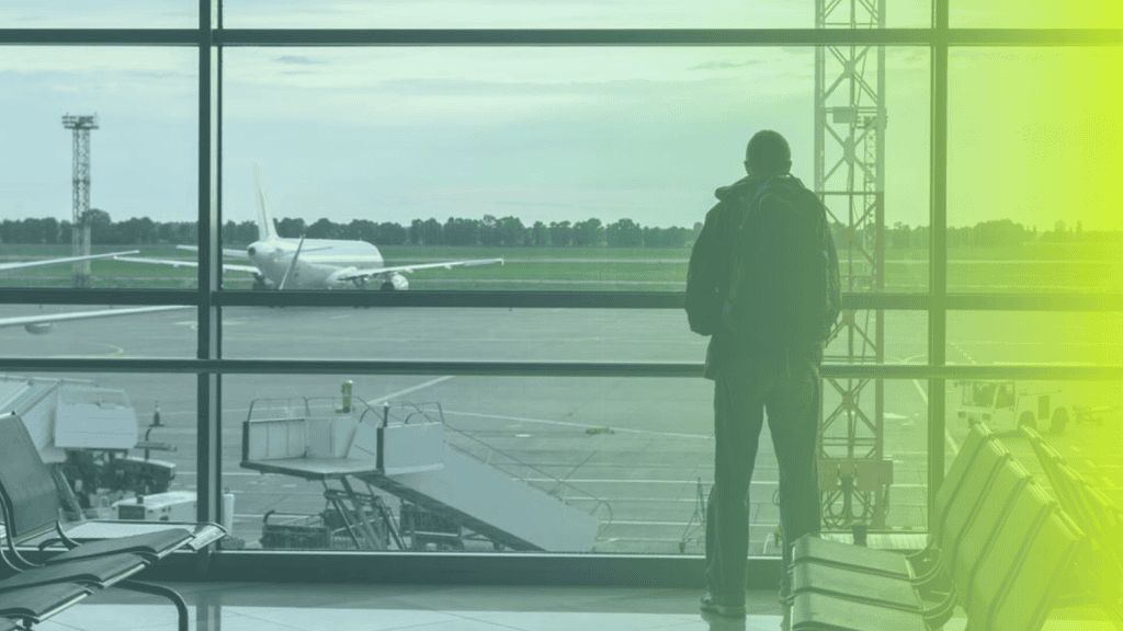 A person with a backpack stands at an airport window, looking out at an airplane on the tarmac; empty seats are visible in the foreground, capturing a quiet moment of reflection and travel—a subtle nod to corporates wellness on the go.