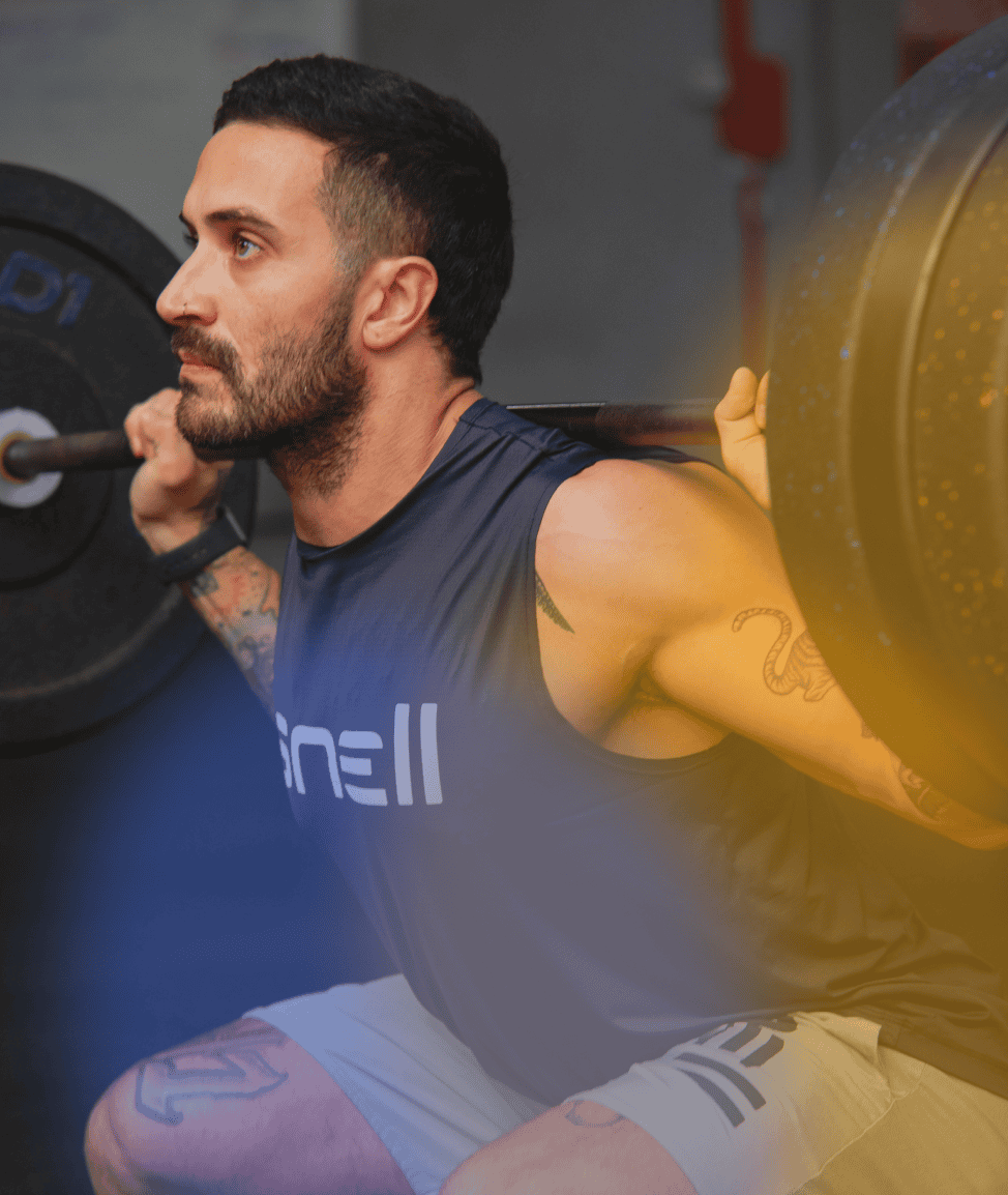 A man in Coya athletic wear performs a barbell squat in a gym, holding the weight across his shoulders with focus and proper form.