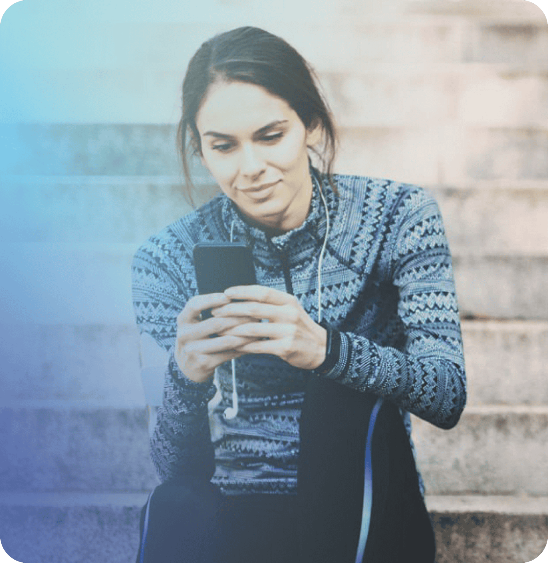 A woman in Coya athletic wear sits on outdoor steps, looking at her smartphone with earphones draped around her neck.
