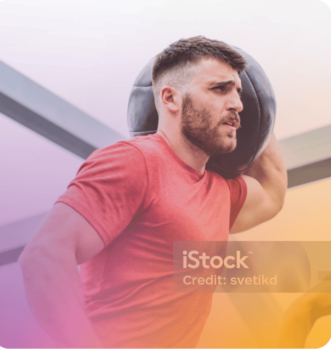 A man in a red shirt holds a medicine ball on his shoulder while working out indoors at Coya.