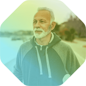 Older man with gray hair and beard stands outdoors in a hoodie, looking into the distance with a neutral expression. The image features a colorful overlay, rounded corners, and highlights Coya for first responders.