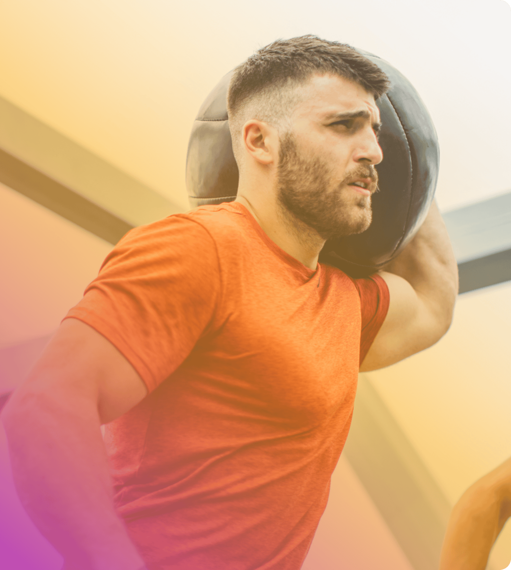 A man in a red shirt holds a medicine ball on his shoulder while exercising indoors, showcasing how coya for fitness clubs supports strength training and active lifestyles.