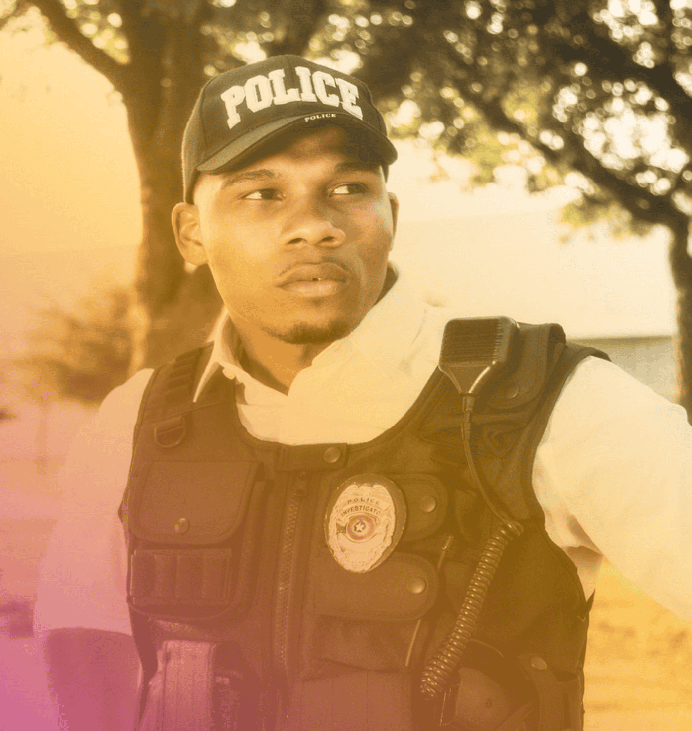 A police officer wearing a black vest and police cap stands outdoors near trees, looking off to the side—ready to respond, powered by Coya for first responders.