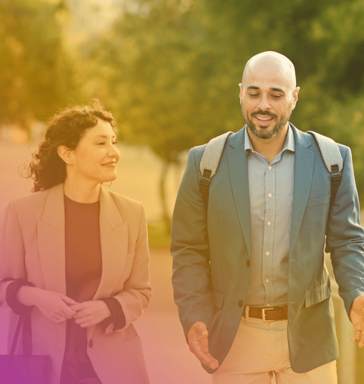 Two people dressed in business attire walk outdoors, engaged in conversation about Coya for companies, with trees and greenery in the background.