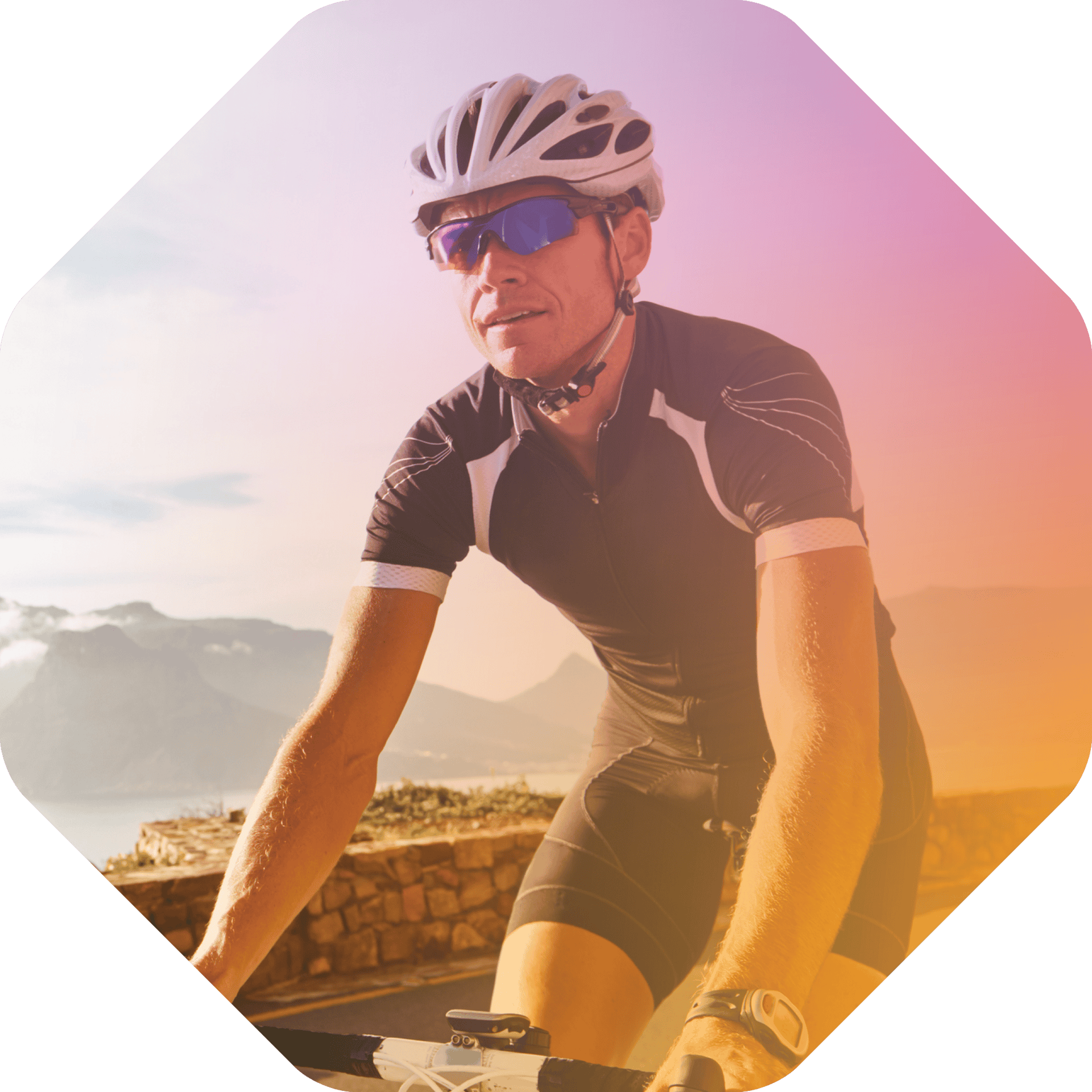 A cyclist wearing a helmet, sunglasses, and cycling attire rides on a paved road near the Coya mountains under a partly cloudy sky.