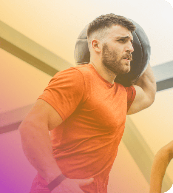 A man in a red shirt holds a medicine ball on his shoulder while working out indoors, showcasing determination and strength—perfect inspiration for a Coya blog post.